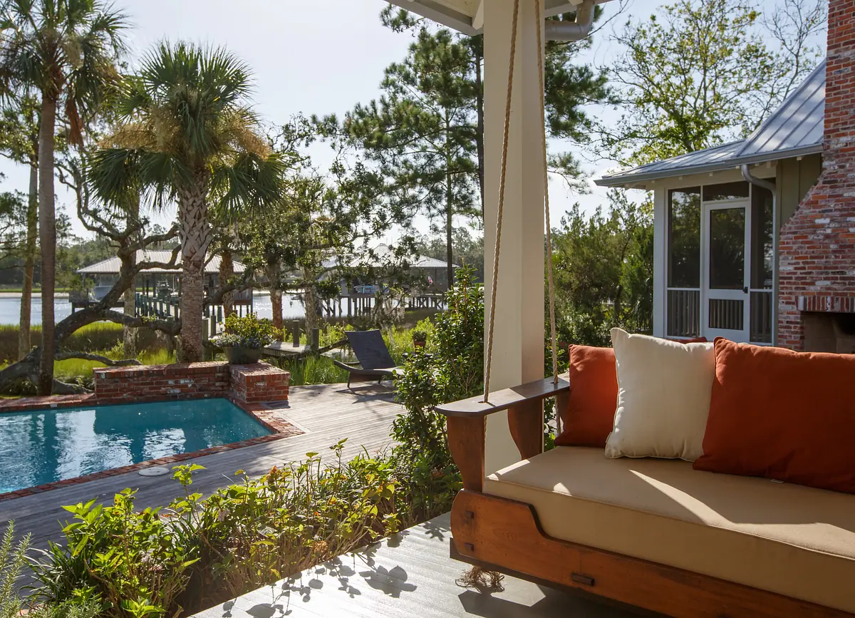 Patio with wooden bench, swimming pool, palm trees, and landscaped greenery overlooking water and dock.
