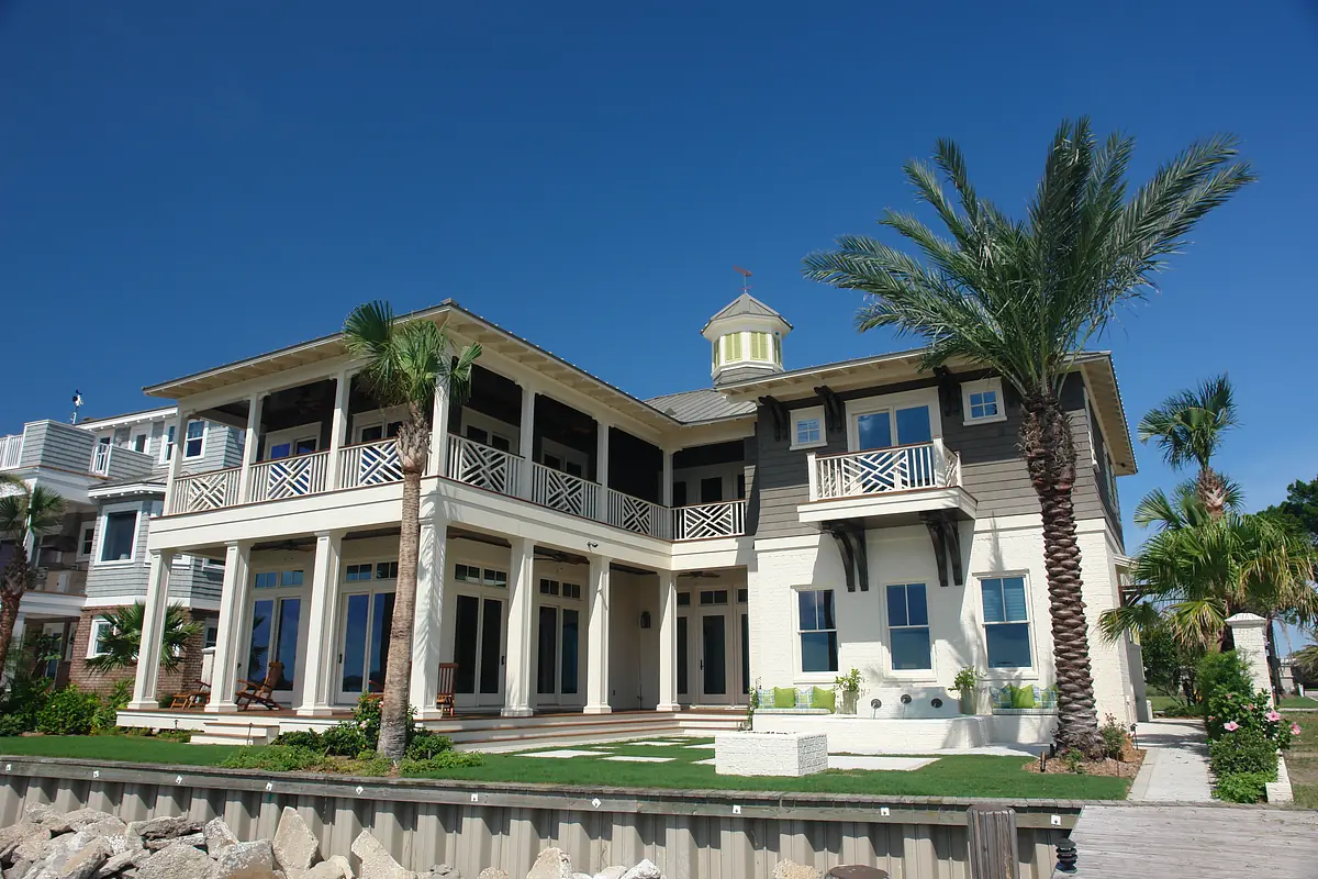 Two-story house with large porch, balconies, palm trees, and stone details.