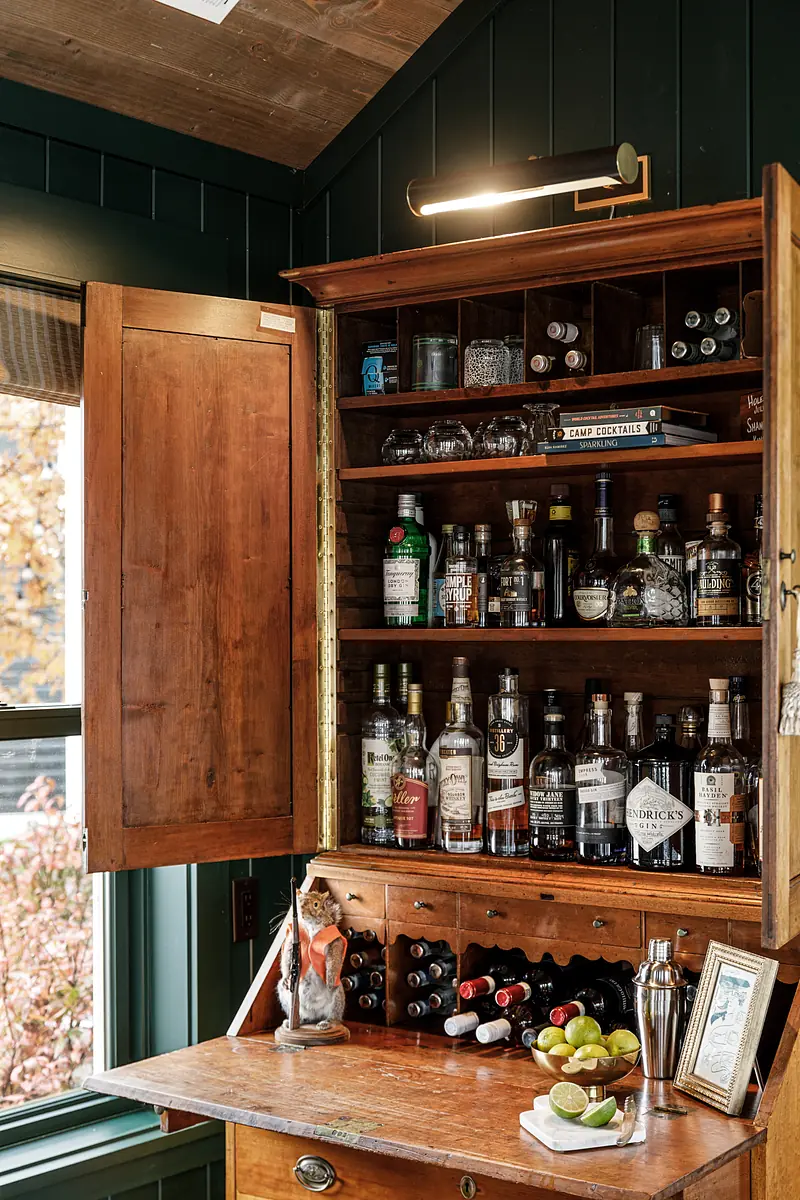 Small bar area with wooden cabinet, liquor bottles, wine storage, countertop with shaker, limes, and figurine.