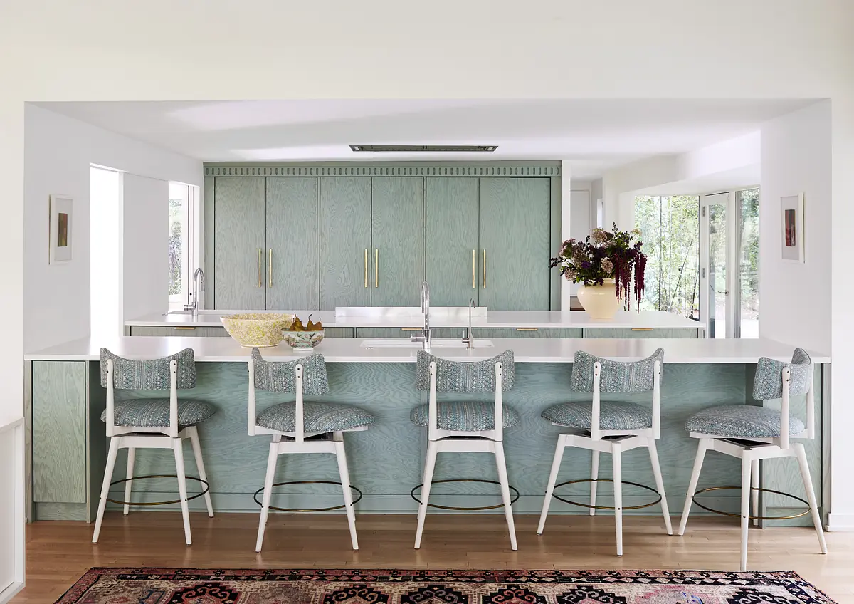 Kitchen with light blue cabinetry, white countertops, bar stools, sink, and decorative flowers.
