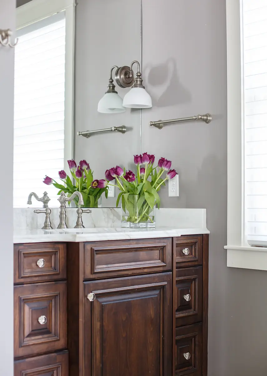 Powder room with dark wood vanity, white countertop, purple tulips, gray walls, and wall sconces for lighting.