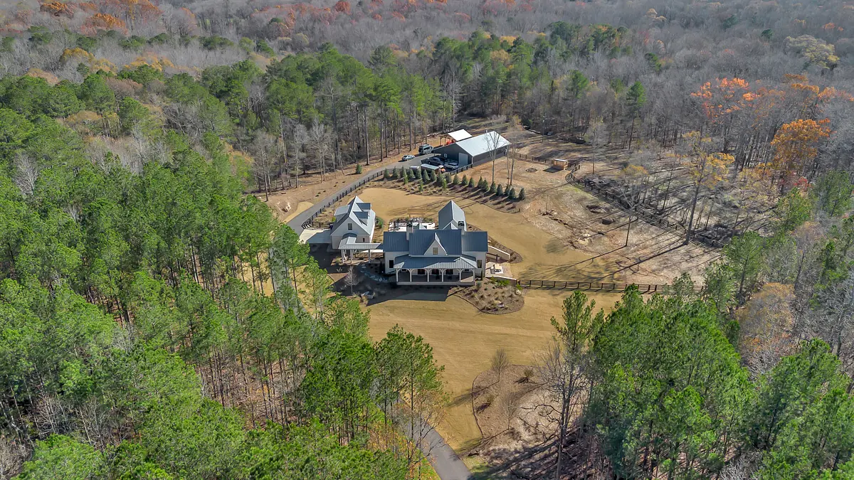 Aerial view of a large estate with multi-level home, porches, trees, and landscaped areas.