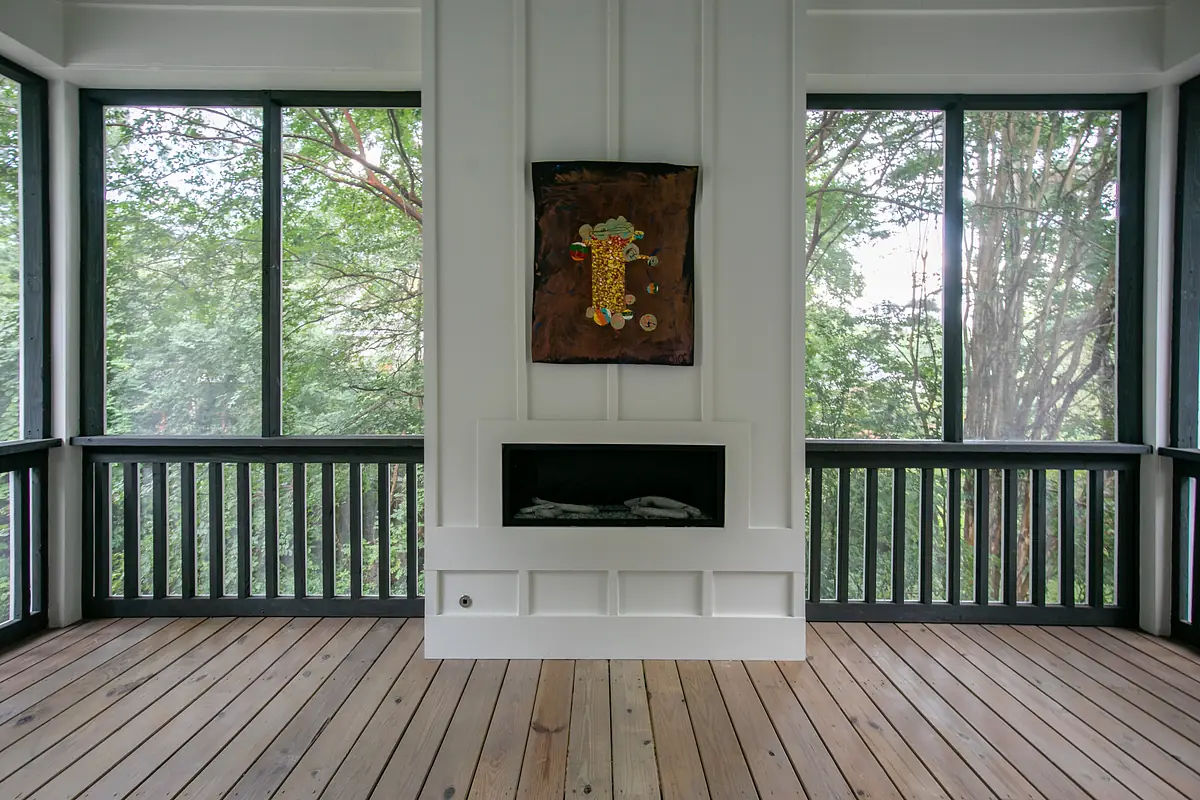 Living room with large windows, black fireplace, wall-mounted artwork, and hardwood flooring.