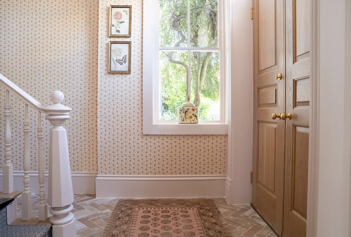 Foyer with patterned wallpaper, wooden door, area rug, staircase, framed artworks, and decorative box