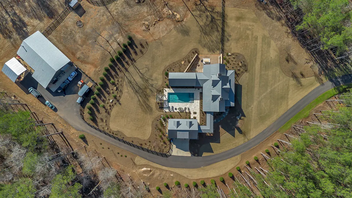 Aerial view of a residential property with main house, swimming pool, patio, and landscaped surroundings.