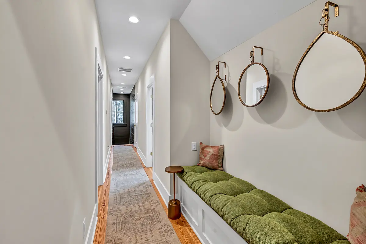 Hallway with green bench, mirrors, side table, patterned rug, and hardwood flooring.