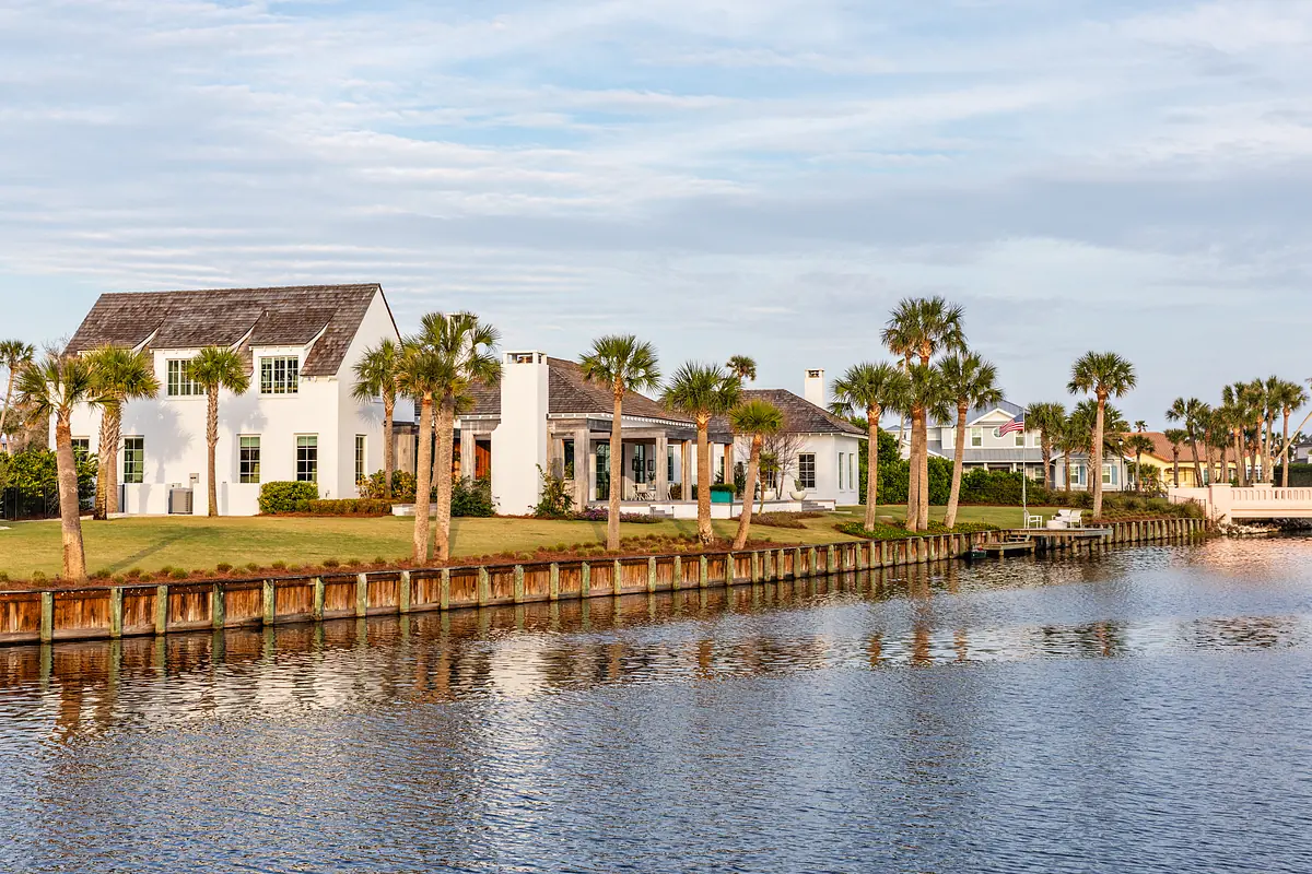 Front exterior view of a white house with palm trees and a waterfront.