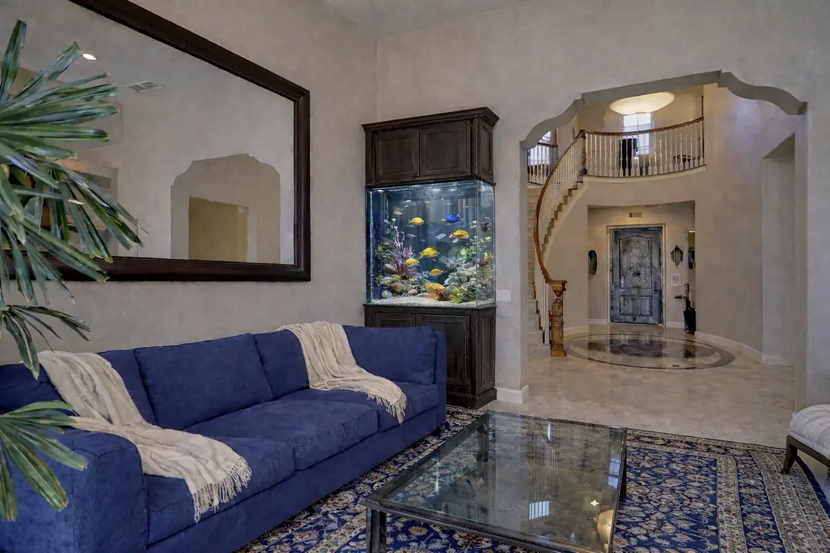 Foyer with blue sofa, glass coffee table, aquarium, staircase, mirror, and decorative archways.