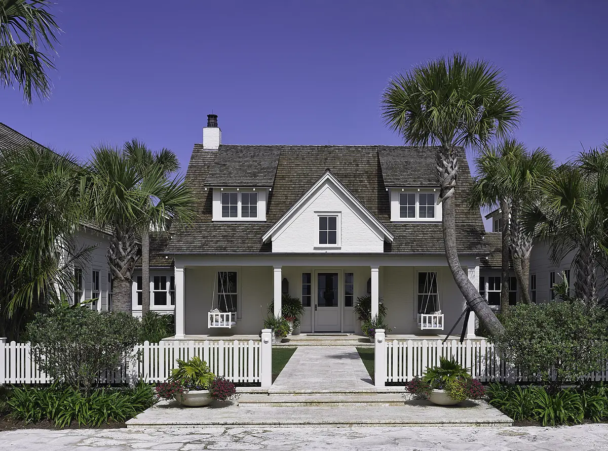 Front exterior of a white two-story house with a porch, palm trees, and a landscaped yard.