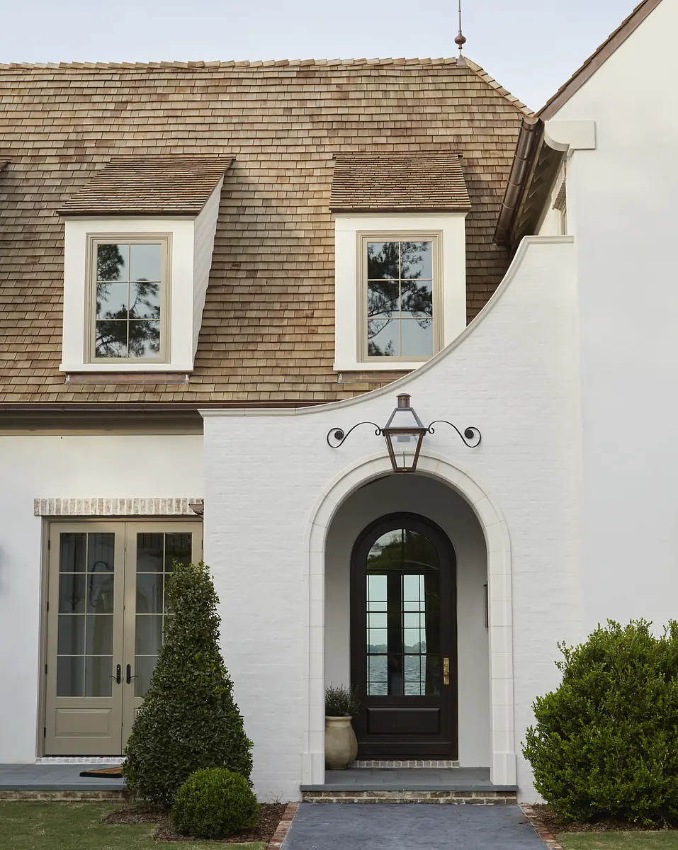 Exterior front view of a house with sloped roof, windows, door, archway, and decorative shrubs.