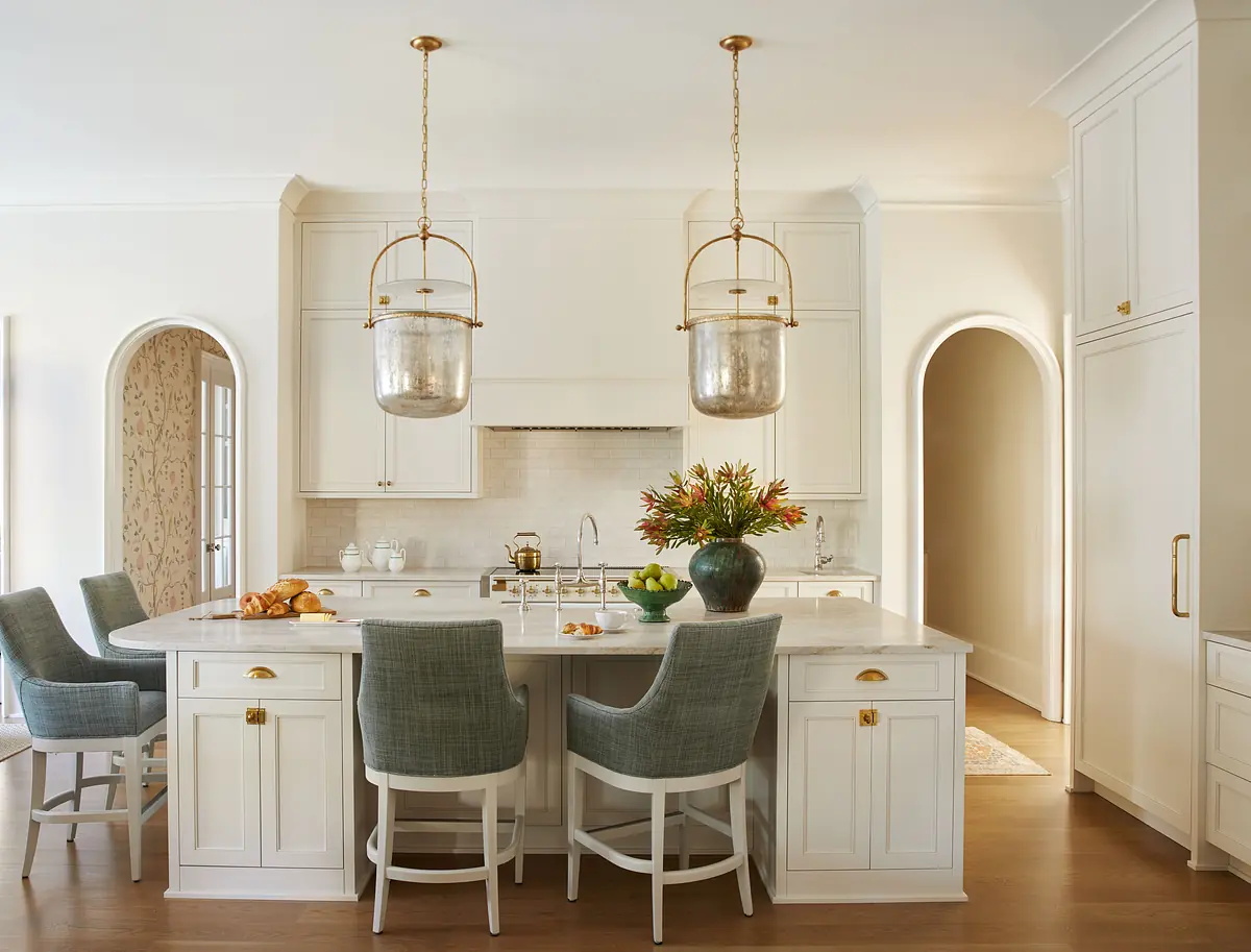 Kitchen with white cabinetry, marble island, four stools, hanging lights, and arched opening.