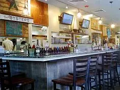Casual dining area with bar counter, high stools, mirrors, TVs, and open kitchen.
