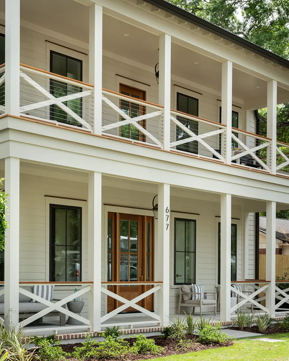 Two-story home with front porch, striped chairs, brown doors, and large windows.