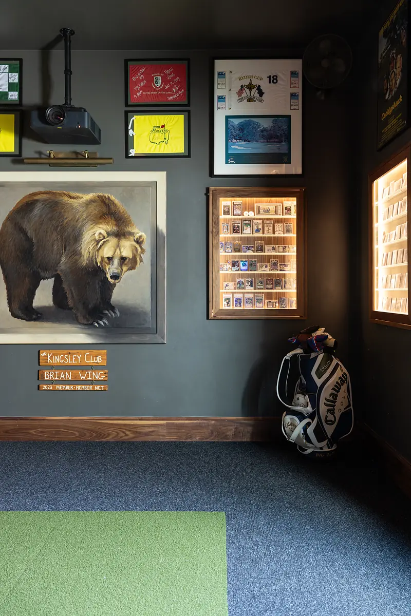 Room with bear painting, display cases, framed artwork, green carpet, and golf bag in corner.