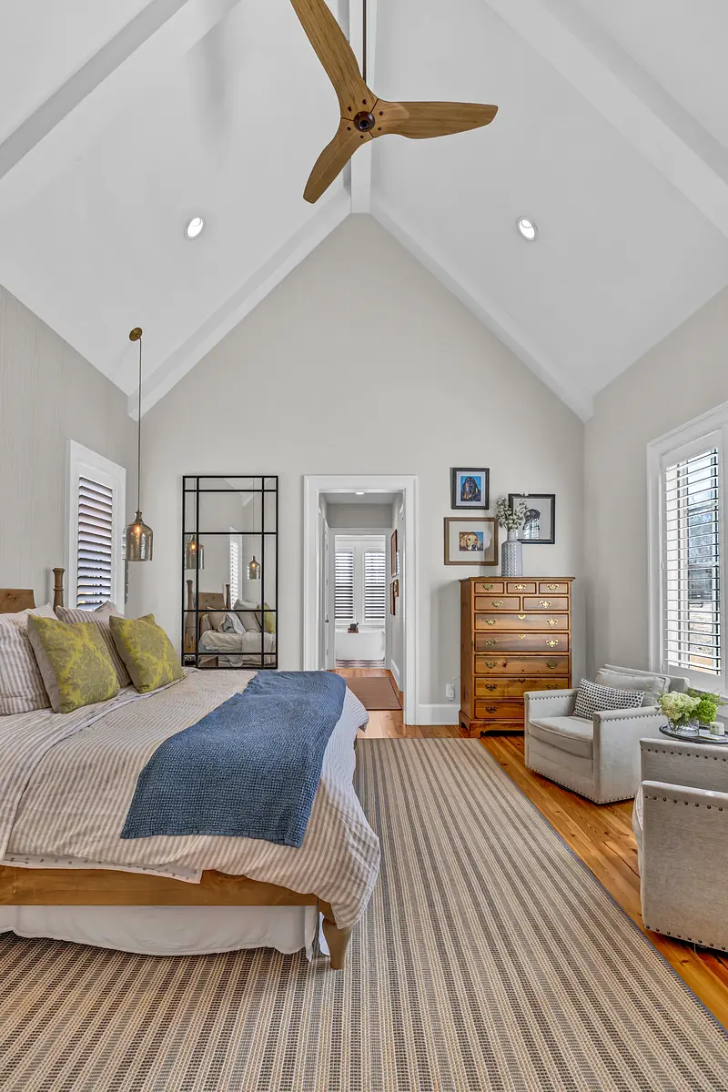 Bedroom with canopy bed, woven rug, armchair, dresser, vaulted ceiling with beams, and ceiling fan.