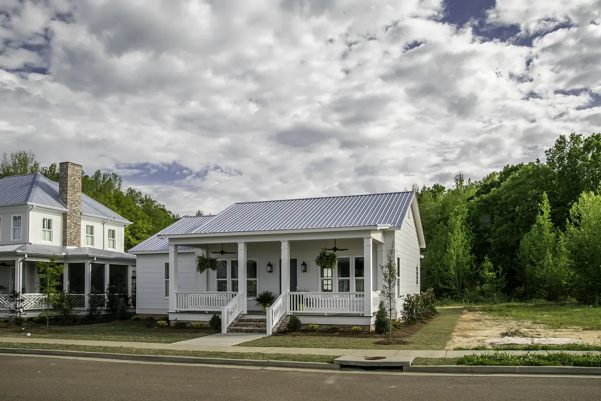 Front exterior of a white house with metal roof, porch, and landscaping.