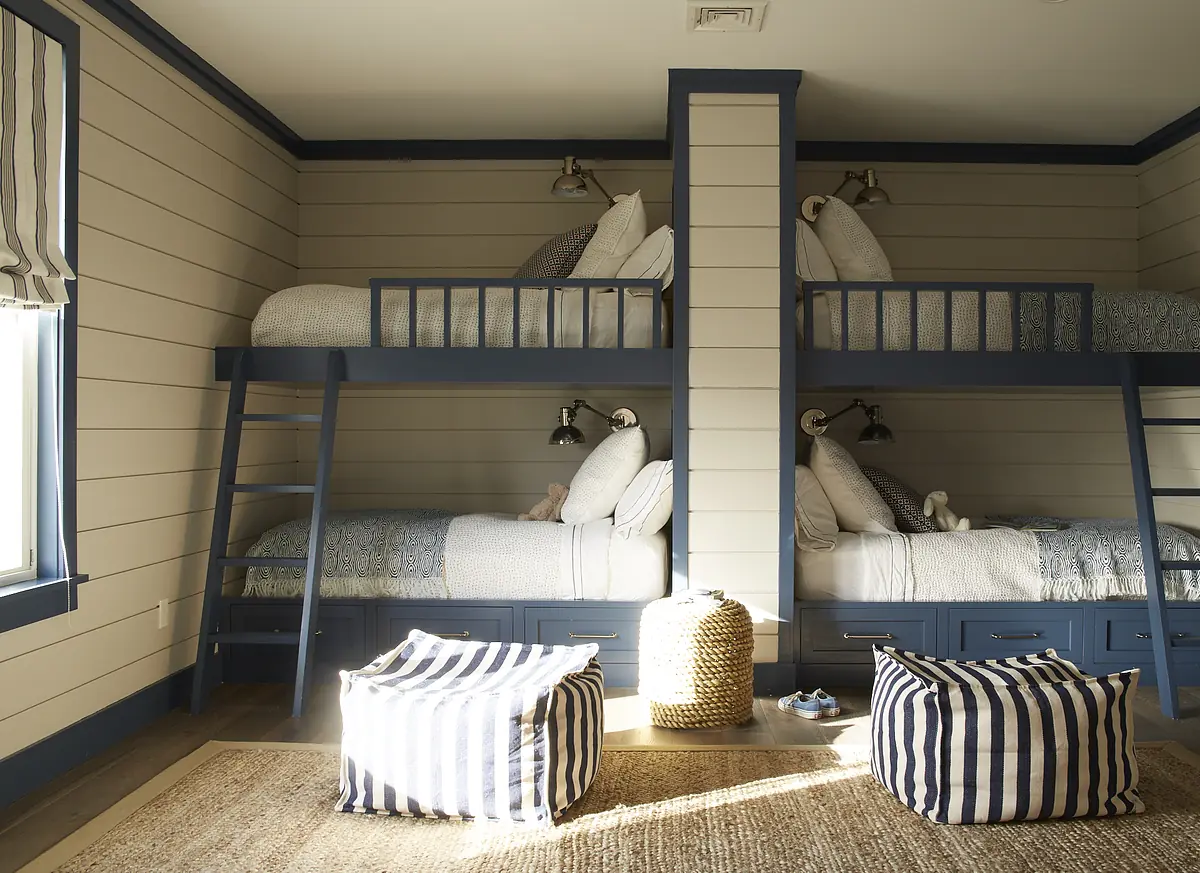 Bedroom with two bunk beds, light bedding, striped poufs, and window with striped shade