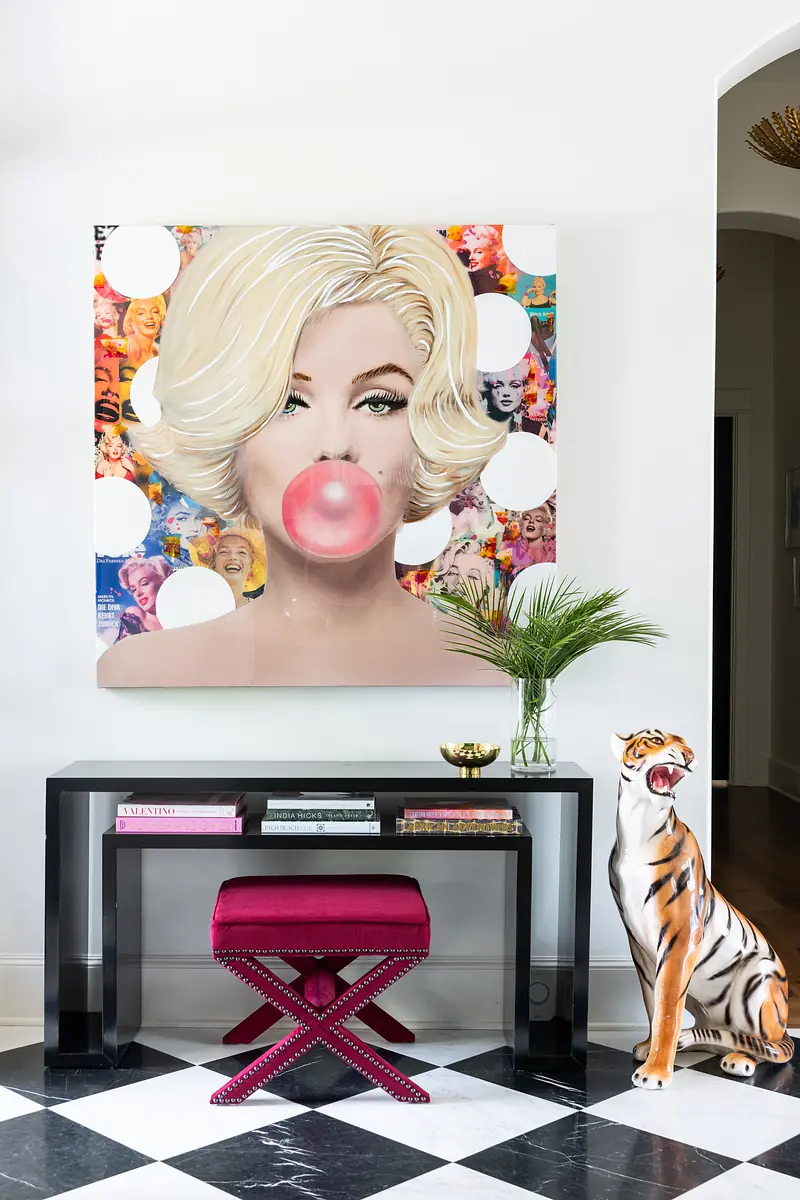 Eclectic arrangement with artwork, black console table, pink stool, and striped tiger sculpture.