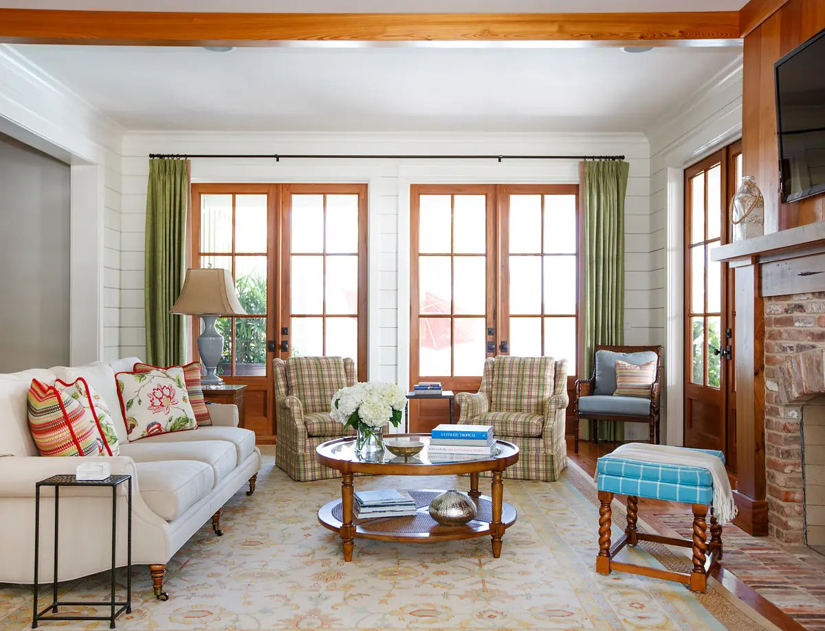 Living room with white sofa, patterned armchairs, coffee table, rug, fireplace, and green curtains.