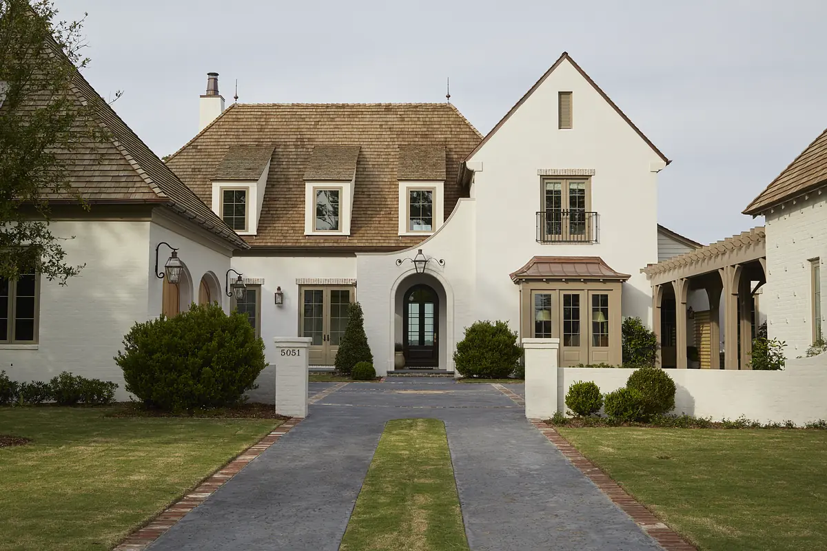 Front exterior of a house with brick pathway, landscaped shrubs, and gabled roofs.