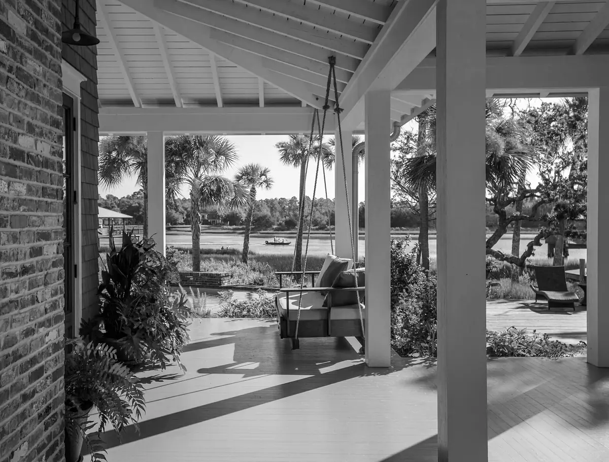 Deck area with swing chair, wooden bench, plants, and view of water body and greenery.