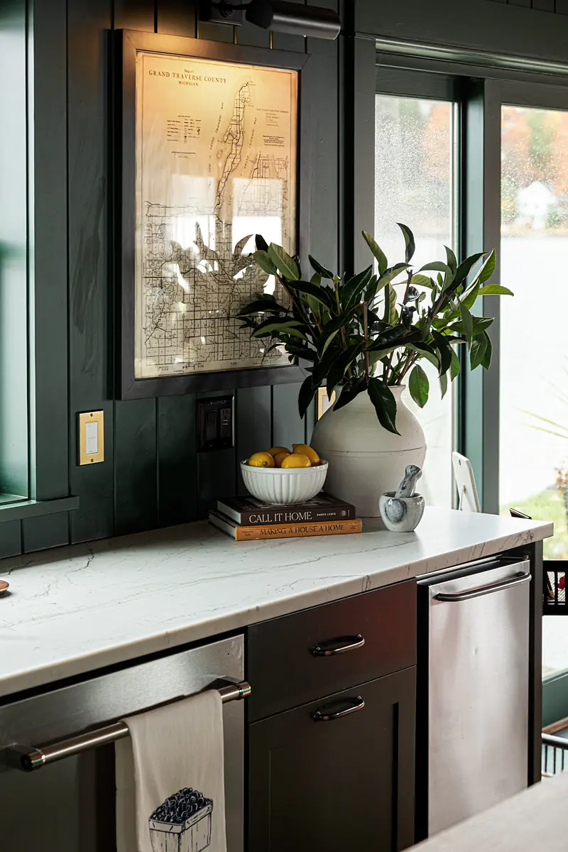 Kitchen with marble countertop, dark cabinetry, large window, framed map, plant, lemons, and books.