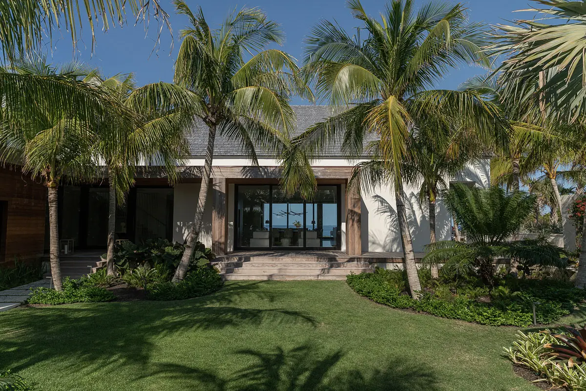 Exterior front view of a modern house with large glass door, palm trees, and landscaped grassy area