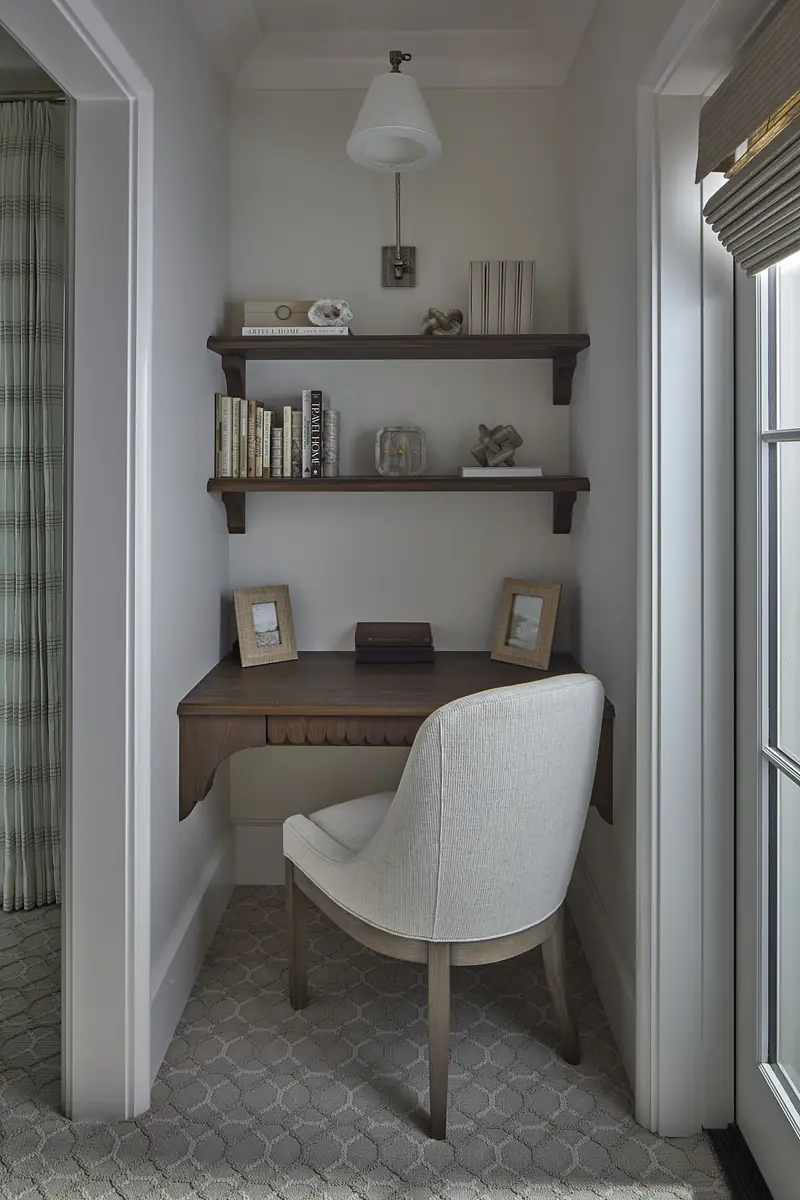 Office nook with wooden desk, gray chair, wall-mounted shelves, books, and framed pictures.