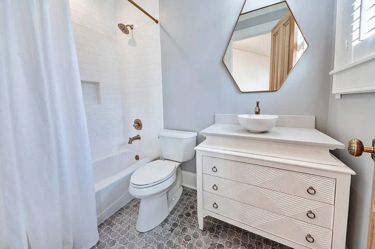 Bathroom with white toilet, wall-mounted sink, decorative vanity, gray mosaic tiles, and a hexagonal mirror.