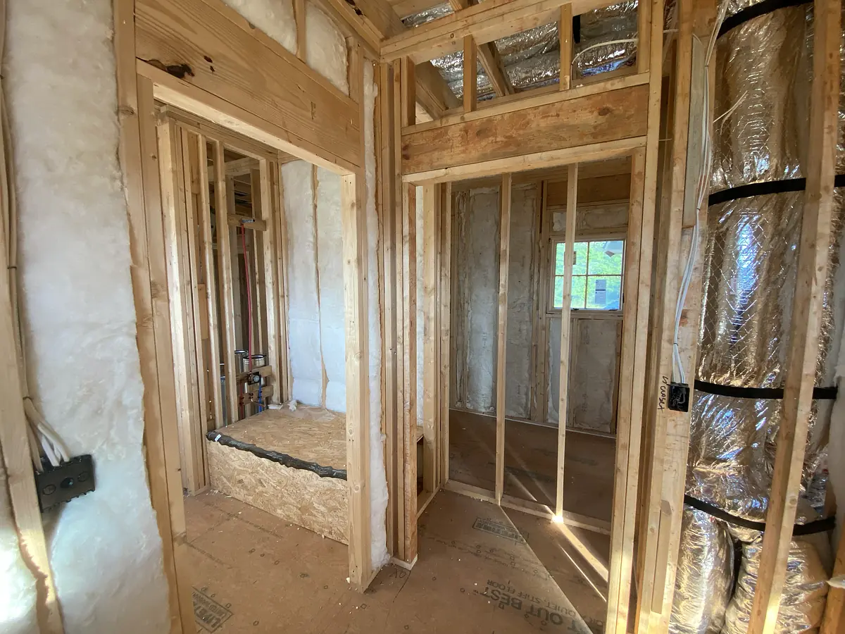 Under-construction space with exposed wooden framing, insulation, and a partially completed shower area.