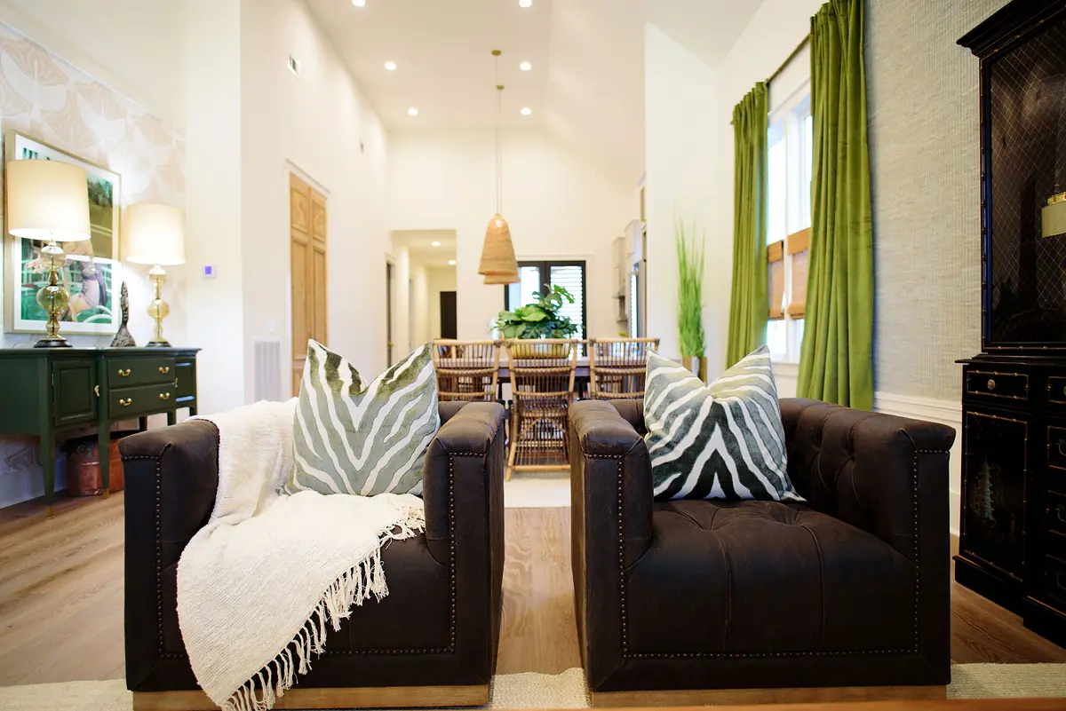 Living room with black armchairs, green side table, dining area, and large windows with green curtains.