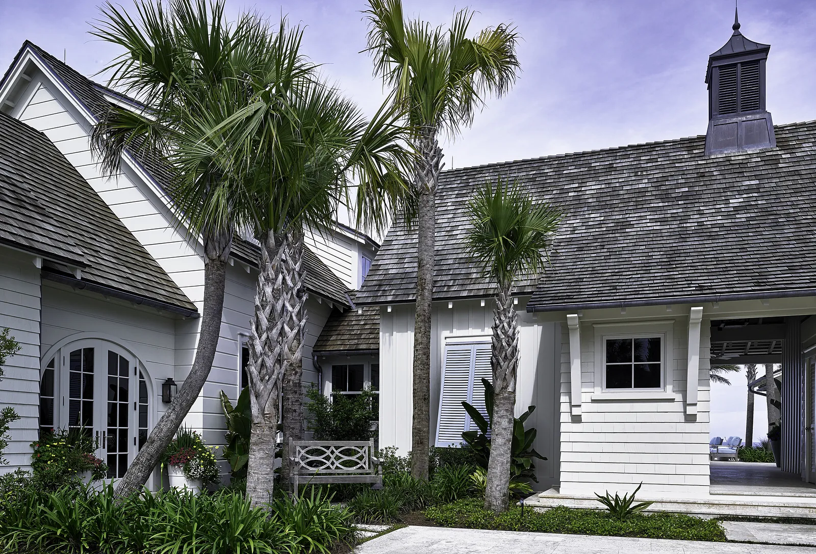 Exterior front view of a house with white siding, palm trees, arched doors, and a stone pathway