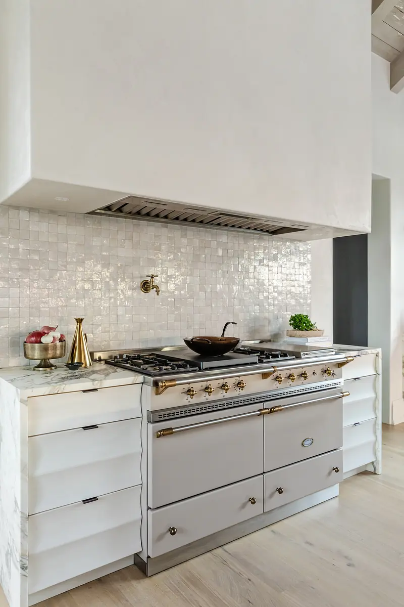 Kitchen with gray stove, white tile backsplash, light cabinetry, and a white countertop with fruit and a plant