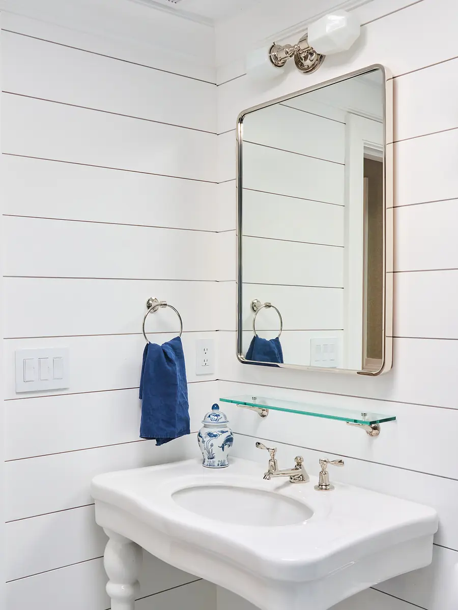 Bathroom with white pedestal sink, glass shelf, mirror, blue towel, and shiplap walls.