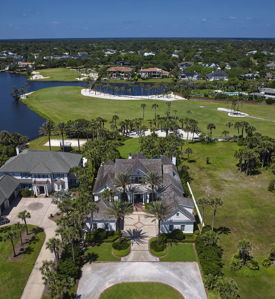 Aerial view of a large house with circular driveway, palm trees, and golf course nearby.