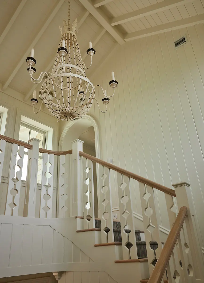 Hallway with wooden staircase, whitewashed walls, large chandelier, and circular motif banisters.