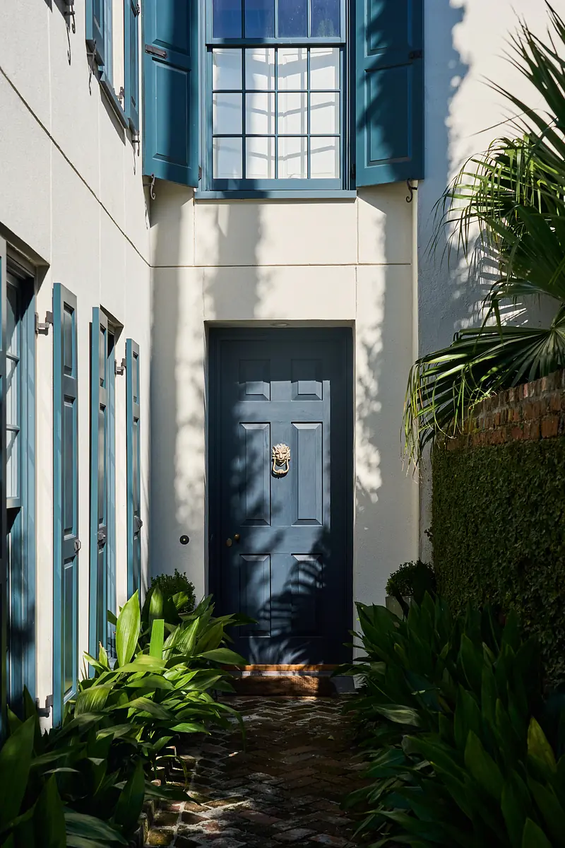 Exterior front view with blue door, shutters, stone path, and green plants.