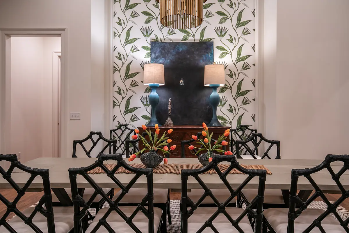 Dining room with long table, eight chairs, flower centerpiece, and leaf-patterned wallpaper.