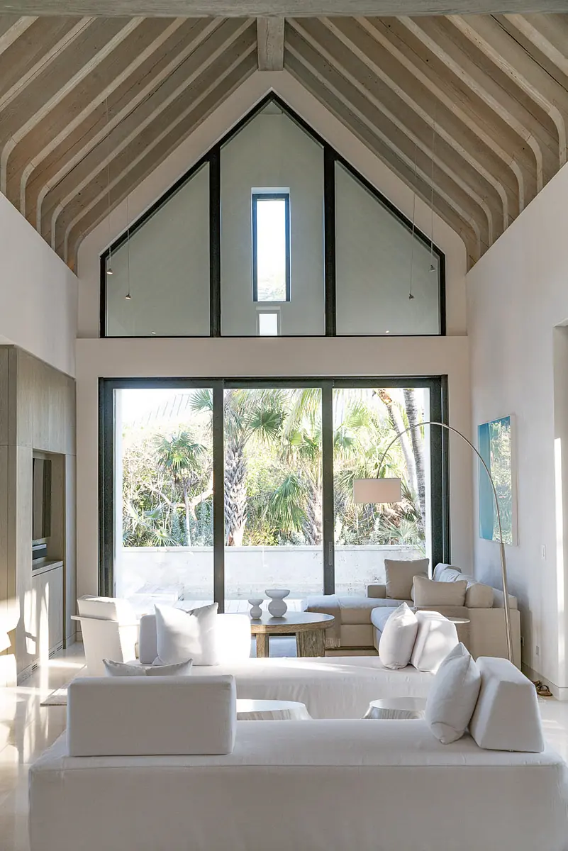 Living room with white sofas, wooden coffee table, curved floor lamp, and large windows overlooking greenery
