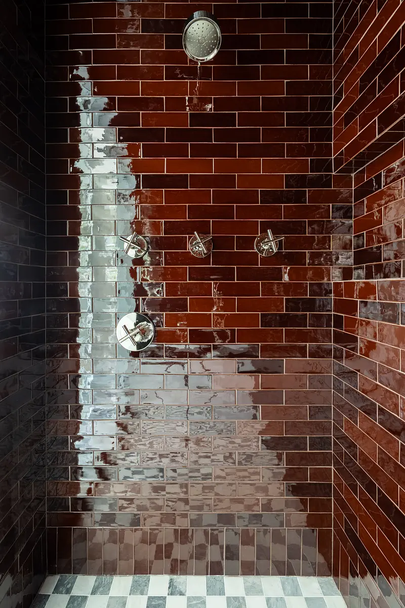 Bathroom with red glossy tiles, rainfall showerhead, multiple controls, and checkerboard black and white floor.