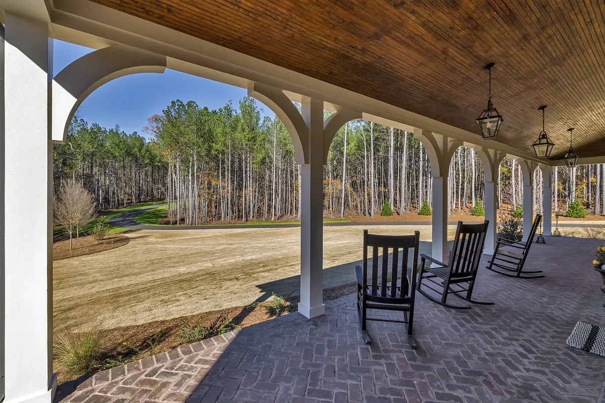 Deck with black rocking chairs, brick floor, and wooden ceiling, open to a forest view.
