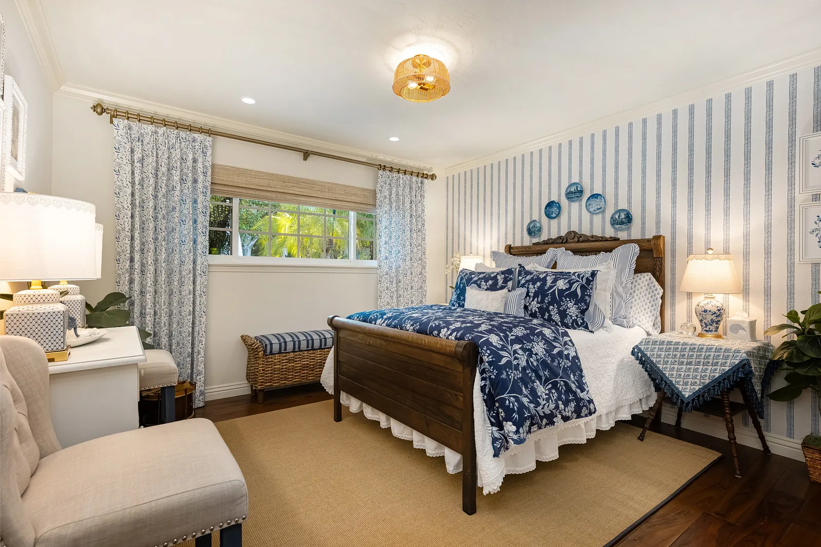 Bedroom with wooden bed, white quilt, blue floral pillows, bedside tables, and blue striped wallpaper