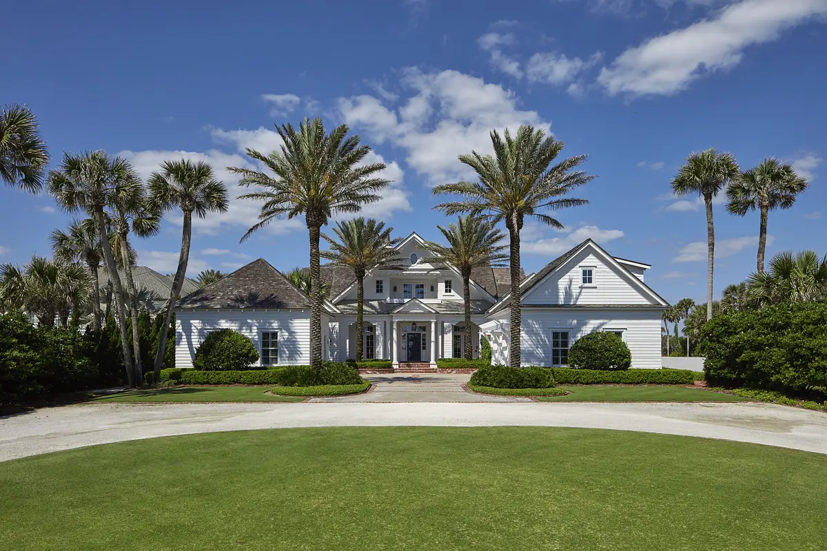 Exterior front view of a house with white siding, gabled roofs, large porch, and palm trees.