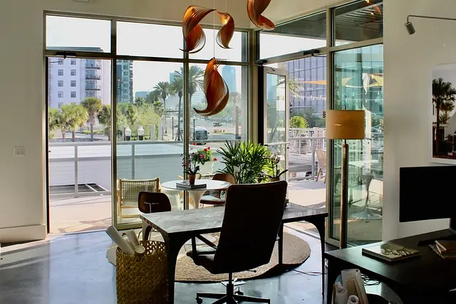 Office with large desk, ergonomic chair, round rug, potted plants, and glass doors leading outside.