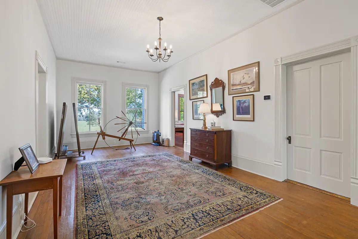 Foyer with hardwood floor, area rug, console table, dresser, artwork, and two large windows.