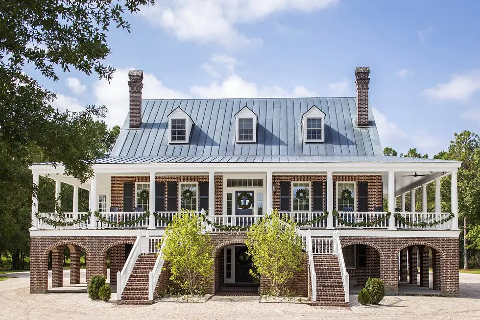 Exterior of a two-story house with gray metal roof, brick walls, large porch, white railings, and green garlands.