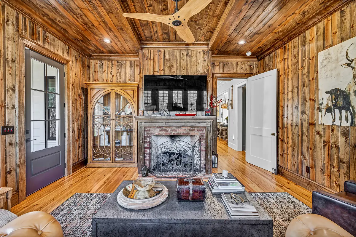 Living room with black coffee table, brown sofa, brick fireplace, wood-paneled walls, and ceiling fan.