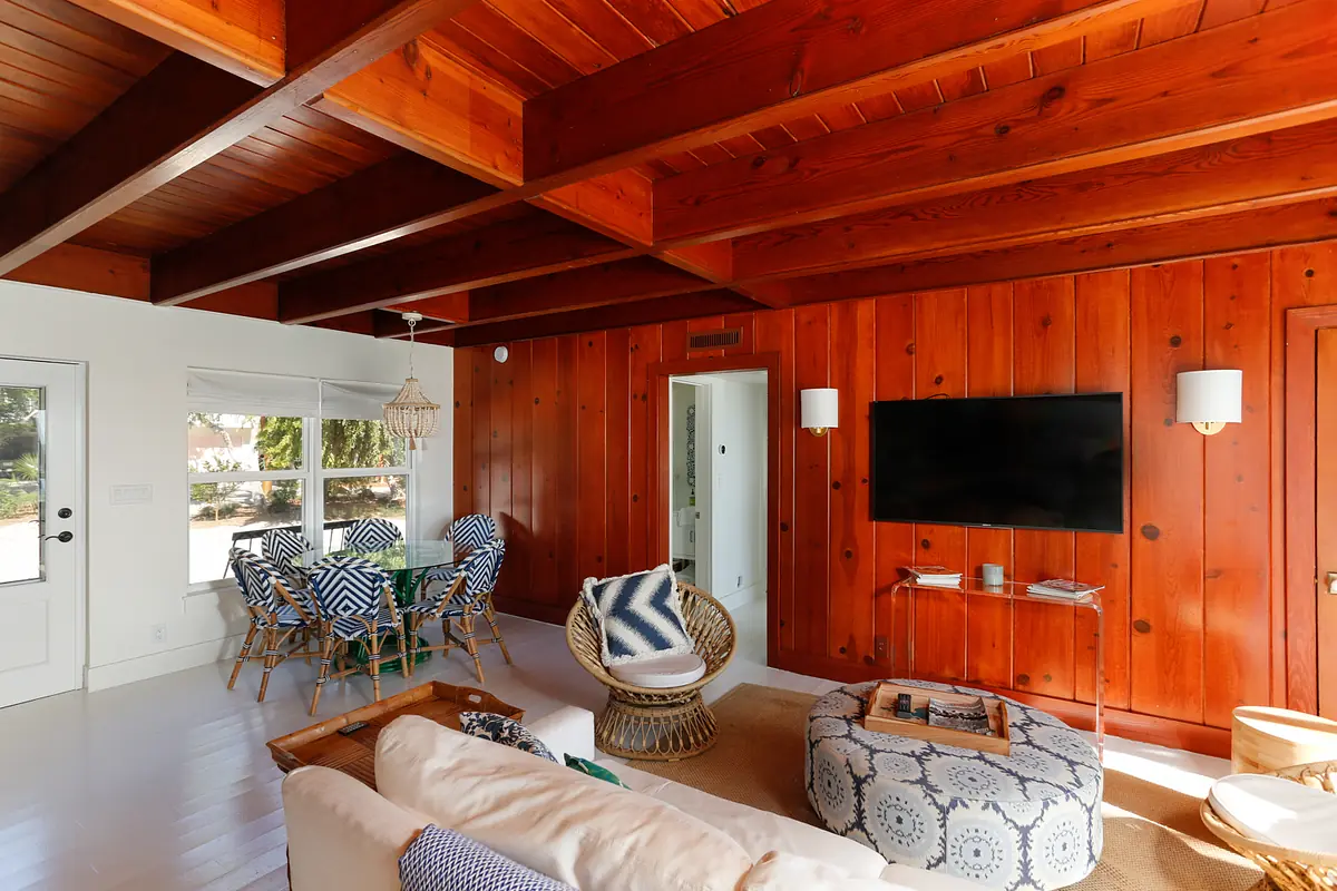 Living room with white sofa, round coffee table, patterned chairs, wood beams, and wooden walls.