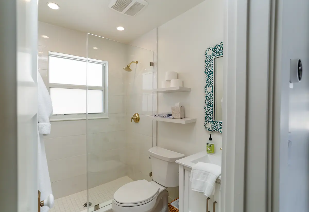 Bathroom with glass shower enclosure, white toilet, cabinet basin, wall-mounted mirror, and shelves.
