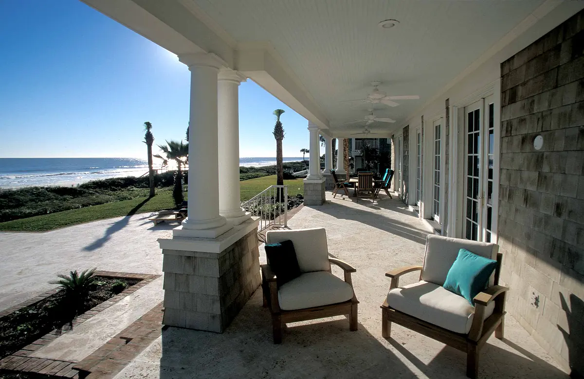 Deck with armchairs, side table, ocean view, stone flooring, and palm trees in the background.